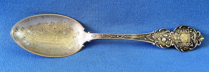 Souvenir Mining Spoon Hecla Mine Burke, ID.JPG - SOUVENIR MINING SPOON HECLA MINE BURKE IDAHO - Sterling silver souvenir spoon, HECLA MINE BURKE engraved in bowl above engraved depiction of mine structure, handle finial has a coat of arms of the State of Idaho in a floral design on both sides and IDAHO written on the neck of the stem, IH on a triangular flag manufacturer’s mark and STERLING in the mold on the back, 5 in. long, 15.1 grams  (Burke was once a thriving silver, lead and zinc mining community located about 7 miles northeast of Wallace, ID.  It’s now a ghost town at the upper end of a string of seven historic mining camps that ran between Gem and Burke in Idaho’s Shoshone County.  Today the town still shows the remains of the massive brick buildings that were once the Hecla Mining Company offices and mine, whose history is intertwined with the town.  With the discovery of rich silver ore, Burke was founded in 1884 as mines and mills were built on the surrounding hillsides of the town’s narrow canyon.  Wooden buildings and a railroad followed within three years and the boomtown was on.   The Hecla Mine was originally discovered by James Toner on May 5, 1885.  His 20-acre silver-lead claim was one of many in the rich Coeur d’Alene Mining District.  He sold it and the mine changed hands several times before it was purchased for $150 by a group of investors in 1891.  These investors led by Amasa B. Campbell, Patsy Clark and John Finch, founded the Hecla Mining Company and incorporated it in the state of Idaho on Oct. 14, 1891.  After seven years of leasing the property, they recapitalized, booted the leasers out and began mining themselves.  They reorganized the company in Washington state on July 12, 1898, electing Amasa B. Campbell as its president and capitalizing the company to $250,000.  In 1900 they were well on their way to profitability, having built up a large surface plant to process their ore.  By the end of 1900, the Hecla Mine produced $229,500 worth of ore.  Just over 15 years after its discovery, the mine became one of the top producers in Burke.  In Oct. 1904, Hecla’s offices were moved from Spokane to Wallace, ID where they remained for over 80 years. Through the economic ups and downs of the first two decades of the 20th Century, the Hecla Mine was a true bright spot, pumping out its silver, lead and zinc treasures.  In 1922, the neighboring Star Mine was purchased by the Hecla Mining Company, and the two mines were then connected by a two-mile long underground tunnel.  Unfortunately, the town of Burke was a disaster waiting to happen.  It was a compact cluster of wooden buildings jammed into the bottom of a narrow canyon.  Because of the narrowness of that hundred-yard wide canyon, the railroad ran through the middle of town.  Most towns had main streets.  Burke had a railroad.  Because of this narrowness, most of the town’s buildings crowded up against the railroad, or spanned over it.  Very few wooden mining towns with Burke’s character escaped the ravages of fire.  On July 13, 1923, the inevitable happened.  Fire ripped through the wooden mass of buildings, quickly burning nearly three-quarters of the town, and reducing the Hecla Mine office and milling complex to ashes.  By the early part of 1925, the town was rebuilt of brick and it was business as usual.  The good times were short lived and the Great Depression and the collapse of zinc prices in the 30s led to the closure of the Star Mine.  The Hecla Mine held on to till 1944 when it too closed after producing nine million tons of ore, yielding 41 million ounces of silver, 732,000 tons of lead and 41,275 tons of zinc, worth some $81 million.  Hecla reopened the Star Mine and continued to expand its operations by purchasing additional mining properties.  Today Hecla Mining Company is the largest primary silver producer in the U.S. through its primary mines, the Greens Creek Mine in Alaska and the Lucky Friday Mine in Idaho.  The company’s expected 2014 silver production is between 9.5 and 10 million ounces.) 